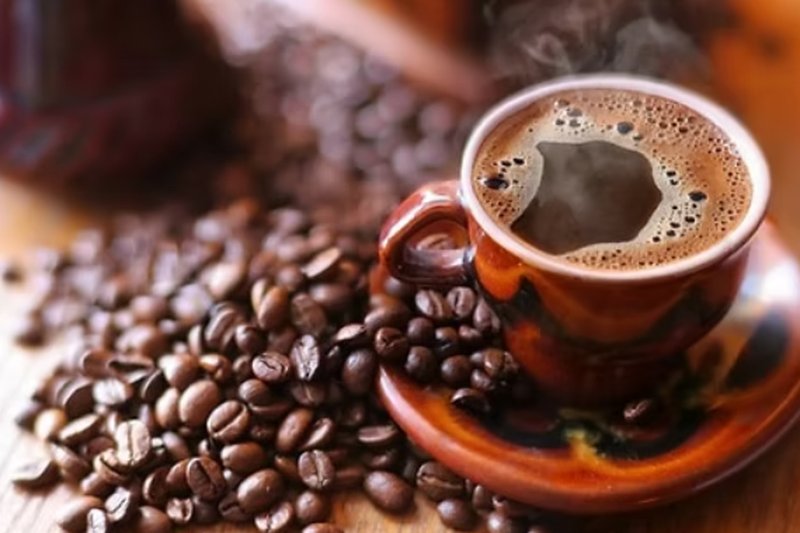 Cangkir kopi Kintamani mengepul di antara biji kopi sangrai