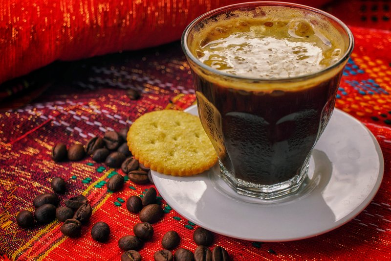 Segelas kopi Gayo panas berbusa dengan biji kopi di sampingnya