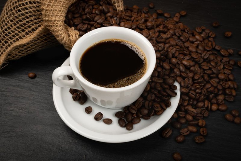 Secangkir kopi Toraja hitam di atas piring putih dengan biji kopi